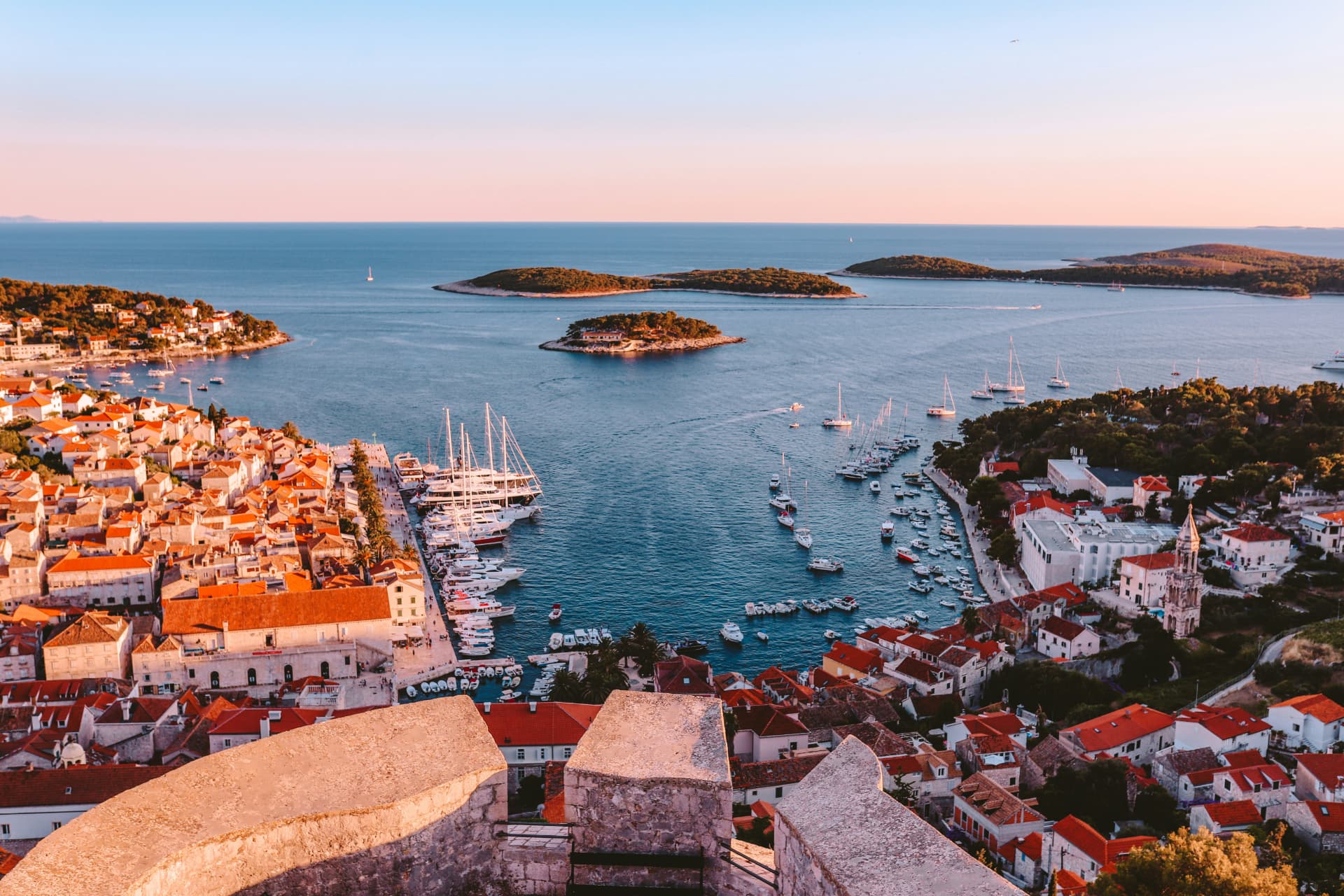 Golden-hour view over Hvar harbour in Croatia, with yachts at anchor and the Pakleni islands beyond