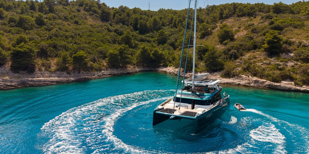 Midori, a Sunreef 70 sailing catamaran, turning in a pine-fringed turquoise cove on the Croatian Adriatic coast